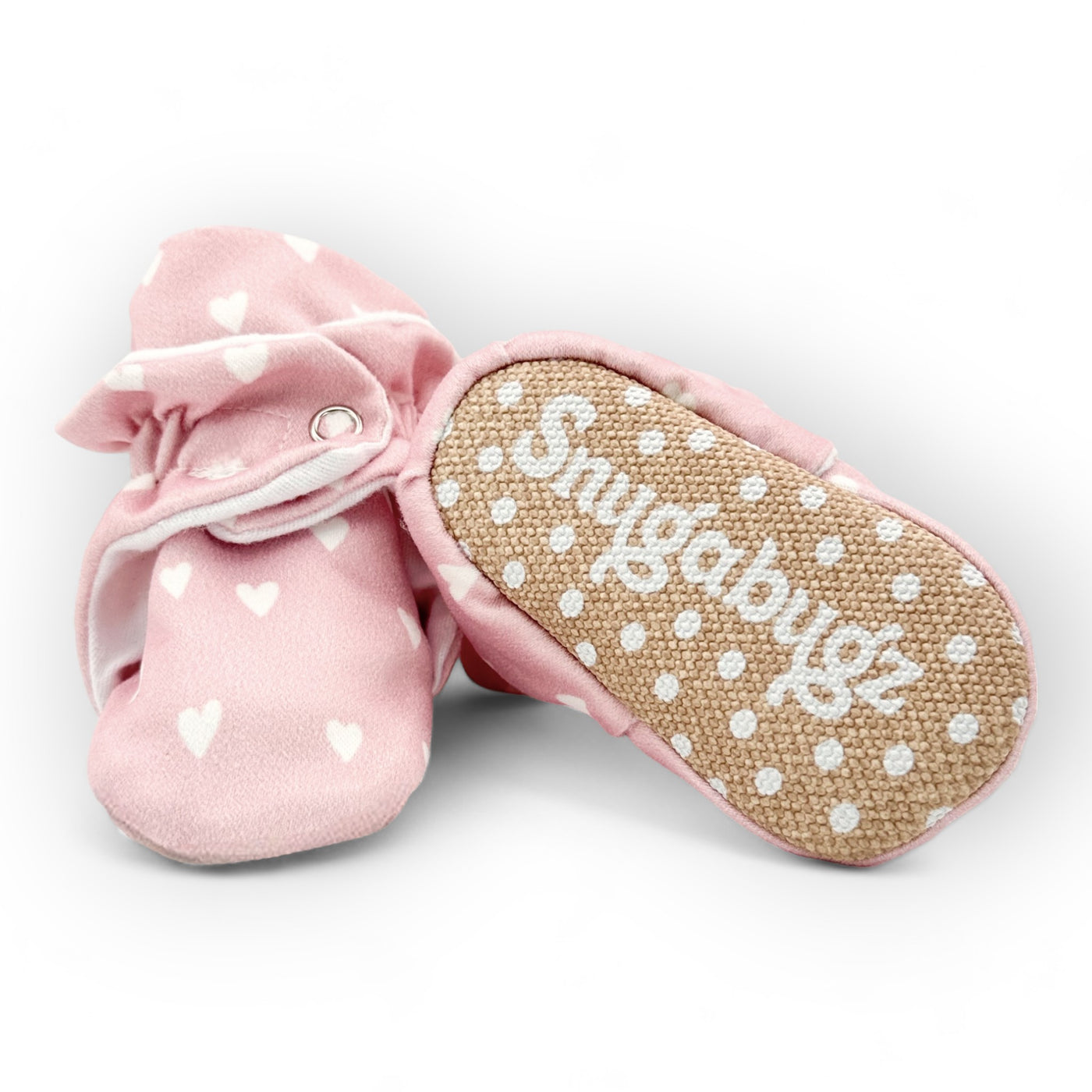 Stay-on baby booties featuring a white hearts print on a pink background, with non-slip soles and adjustable three snap closure. Made from organic cotton.