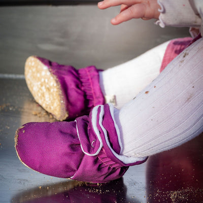 Purple water-resistant baby pre walker booties shoes with non slip soles on a child's feet on a slide in a playground