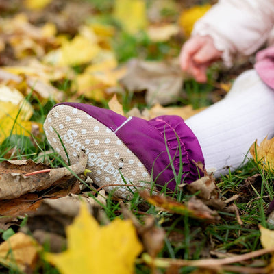 Purple water-resistant baby pre walker shoes with non slip soles on a child's foot, on grass and leaves