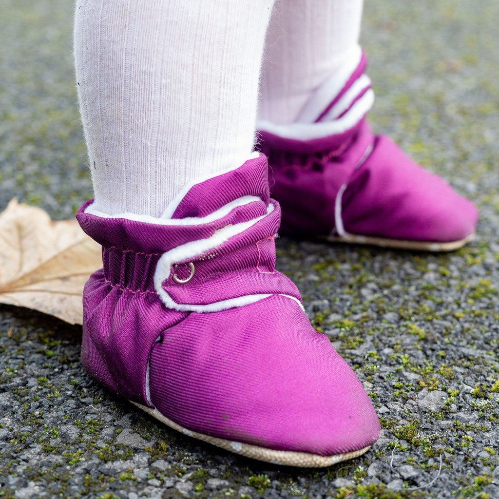 Purple water-resistant baby pre walker shoes with non slip soles on a child's feet, standing on a pavement surface.