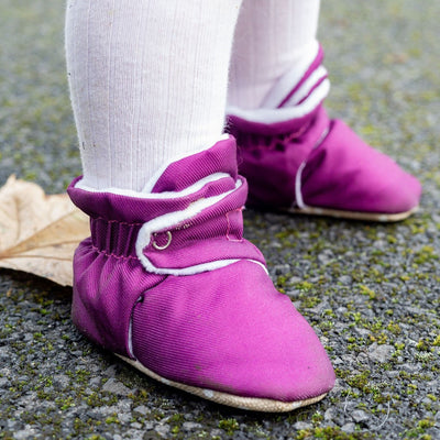 Purple water-resistant baby pre walker shoes with non slip soles on a child's feet, standing on a pavement surface.