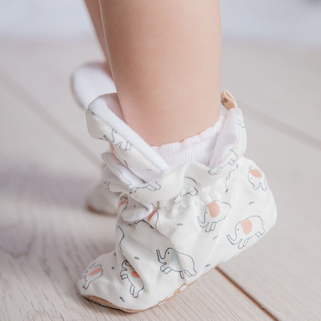White stay-on baby booties that stay on featuring a neutral elephant print, with non-slip flexible soles and adjustable snap closure. Barefoot Baby Shoes. organic cotton baby booties. gender neutral Pram slippers that stay on. sock booties. toddler slippers. indoor baby shoes