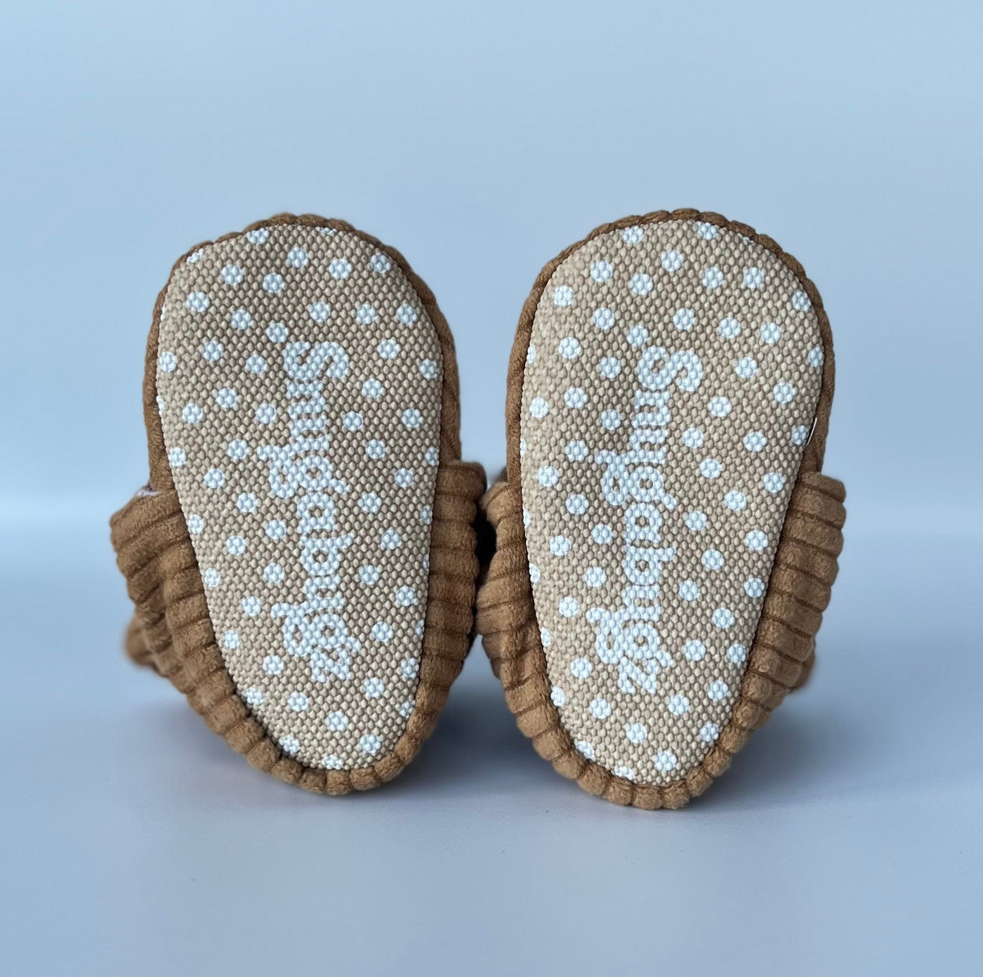 Pair of brown corduroy baby booties with anti slip soles on a white background